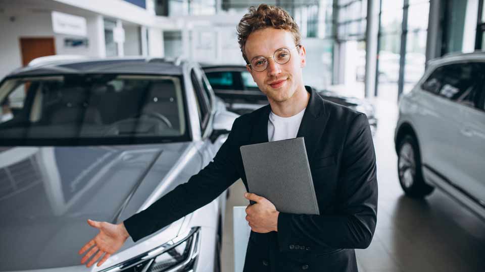 Ein Verkäufer zeigt auf ein Auto und erklärt dem Kunden die Konditionen beim Auto verkaufen Köln
